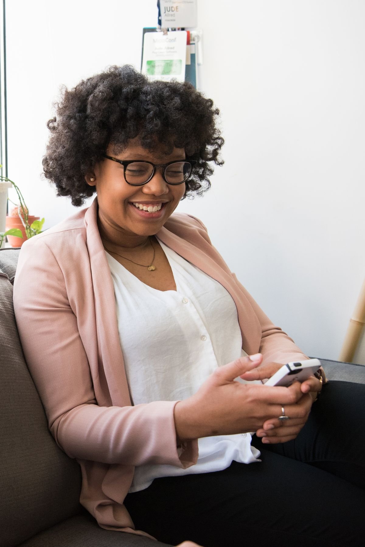 Smiling woman in a pink cardigan holding her phone while sitting on a couch