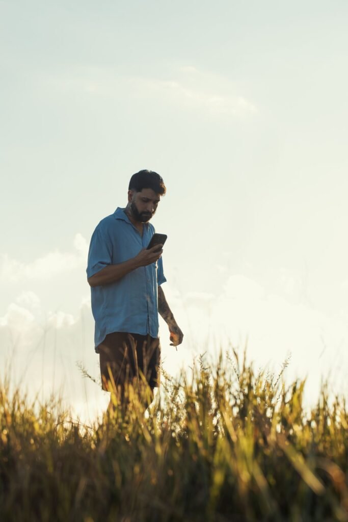 Man checking his phone outdoors in a field at sunset