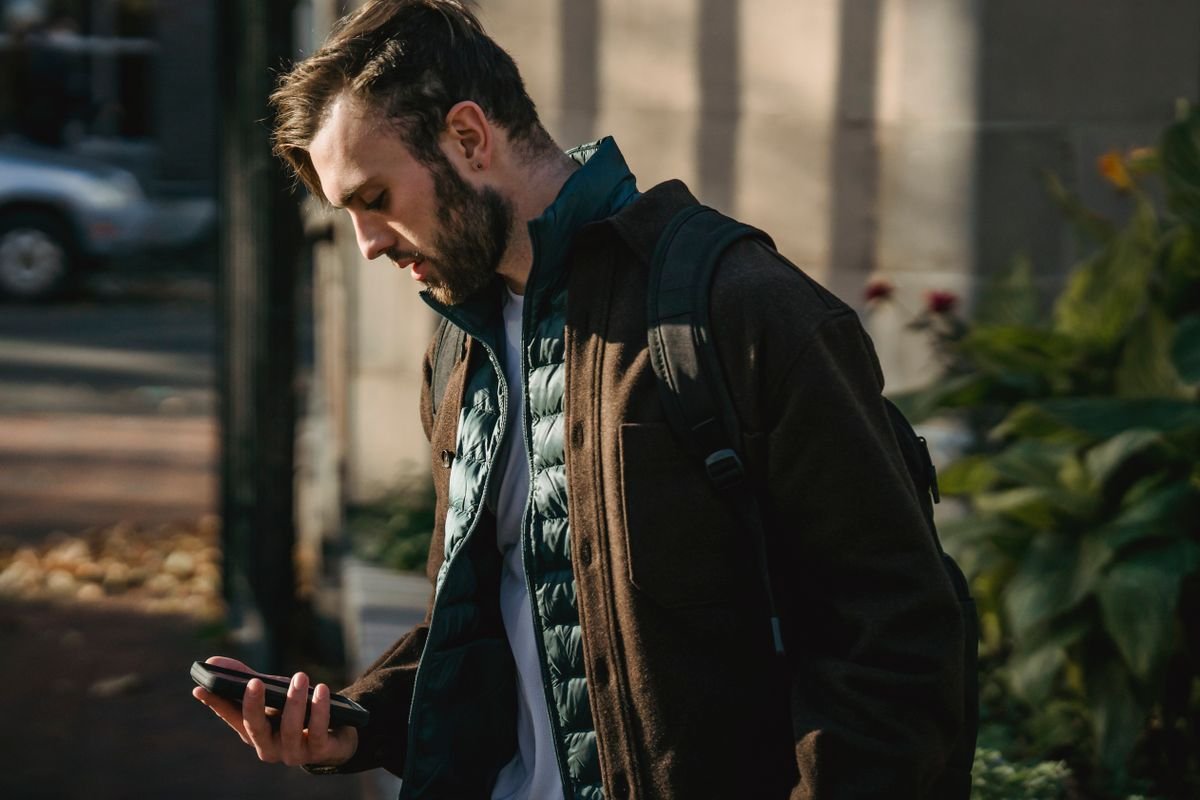Guy casually using his phone while walking on a city street