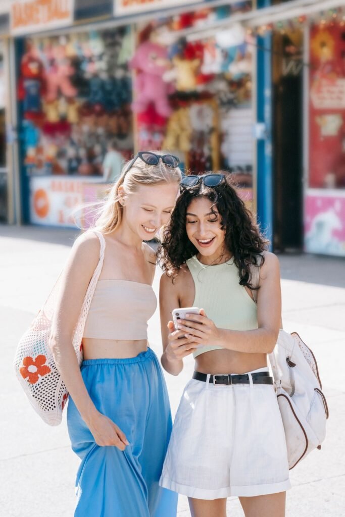 Two smiling girls using a cellphone together on the street