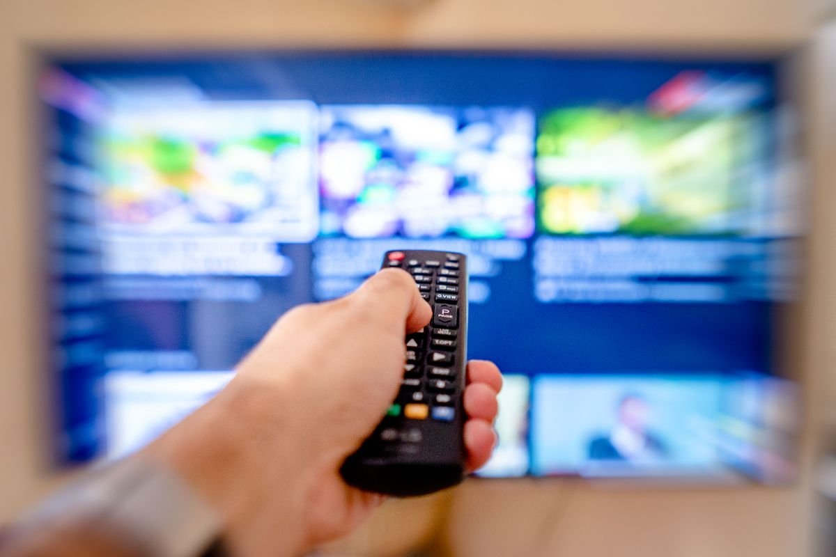 Close-up of a hand pointing a remote control at a TV screen