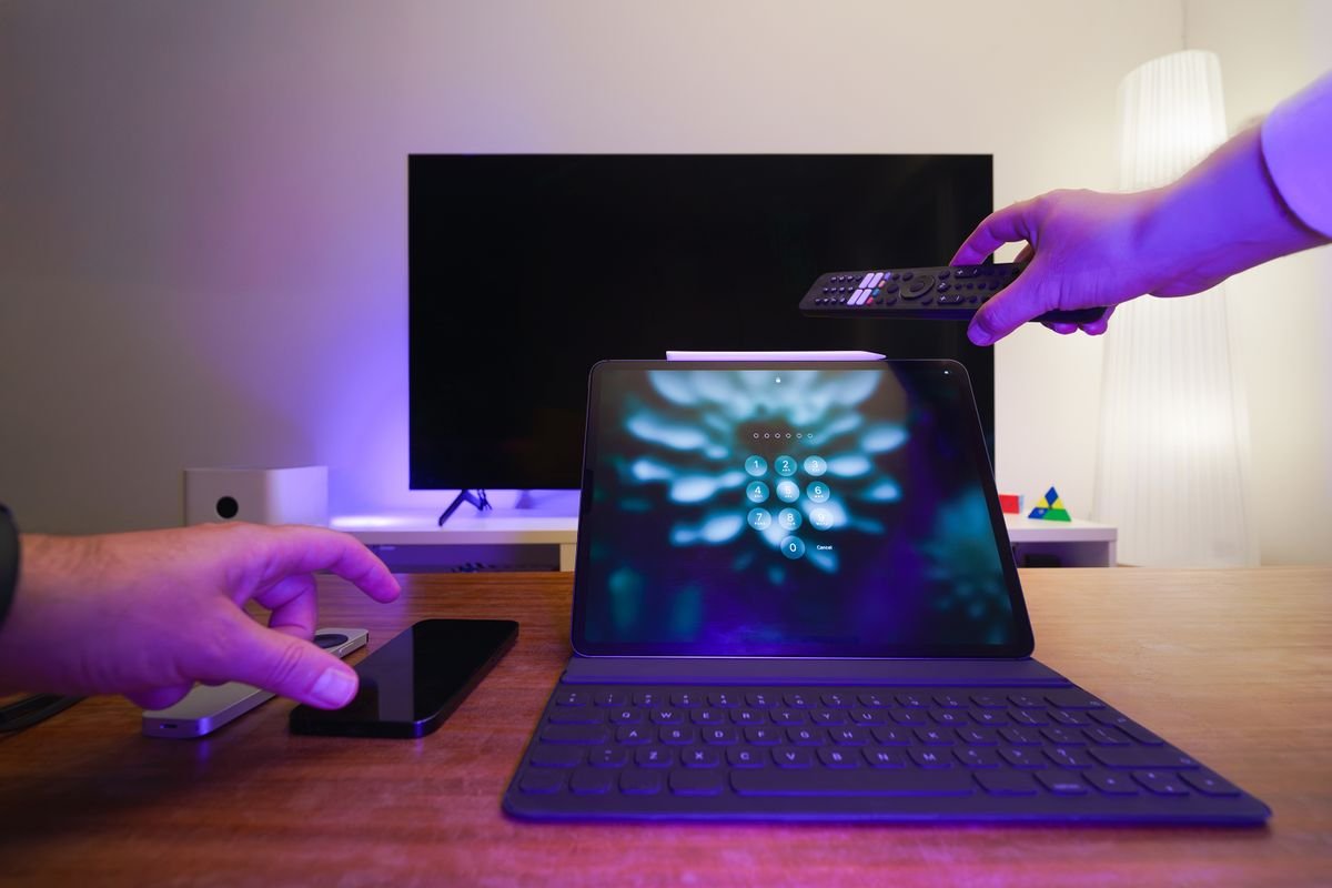 Hands holding a remote control and a tablet in a modern living room with a TV
