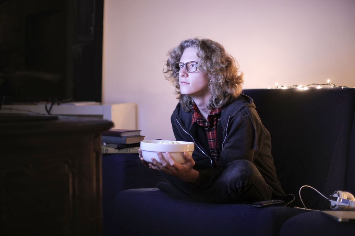 Person sitting on a couch watching TV while holding a bowl of popcorn