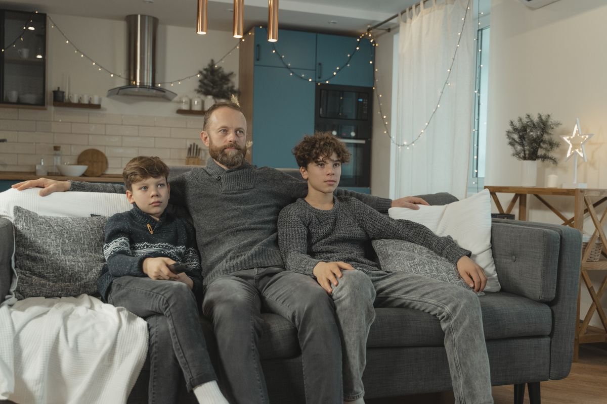 Father and his two children watching TV together on a cozy sofa